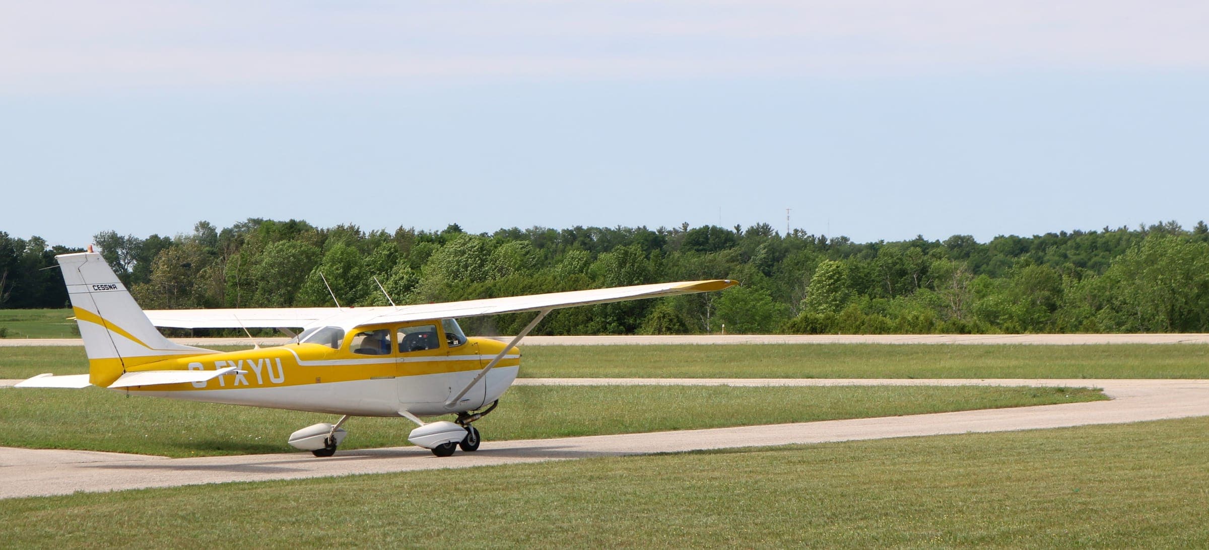 A yellow and white Cessna taxiing past the grass to the runway.